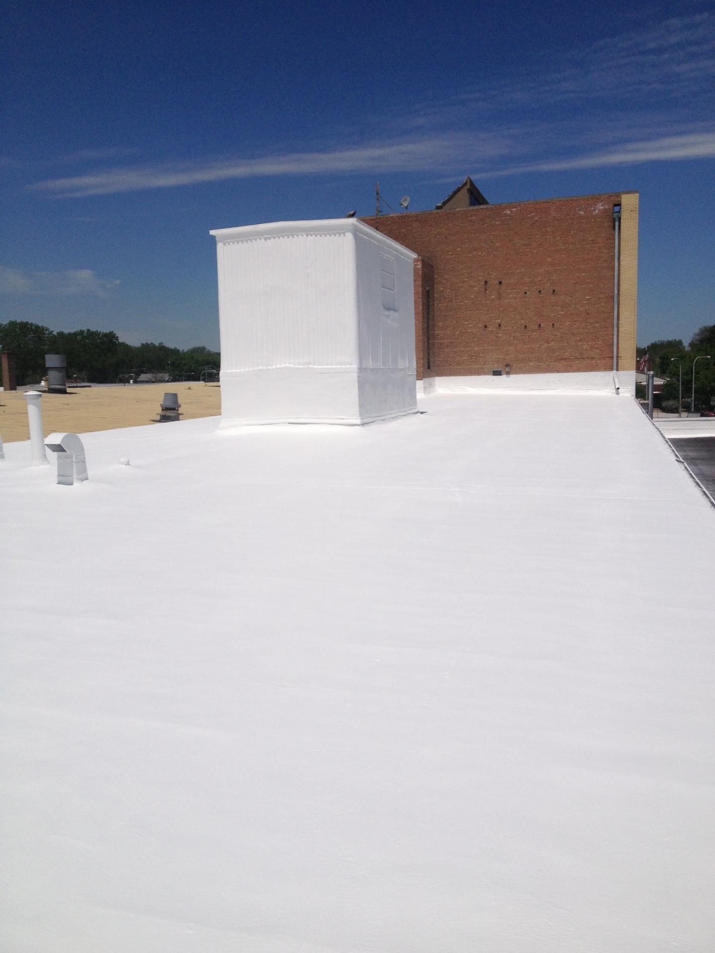 Finished seamless white roof coating on a low-slope commercial roof, continuing up and over the rooftop curb
