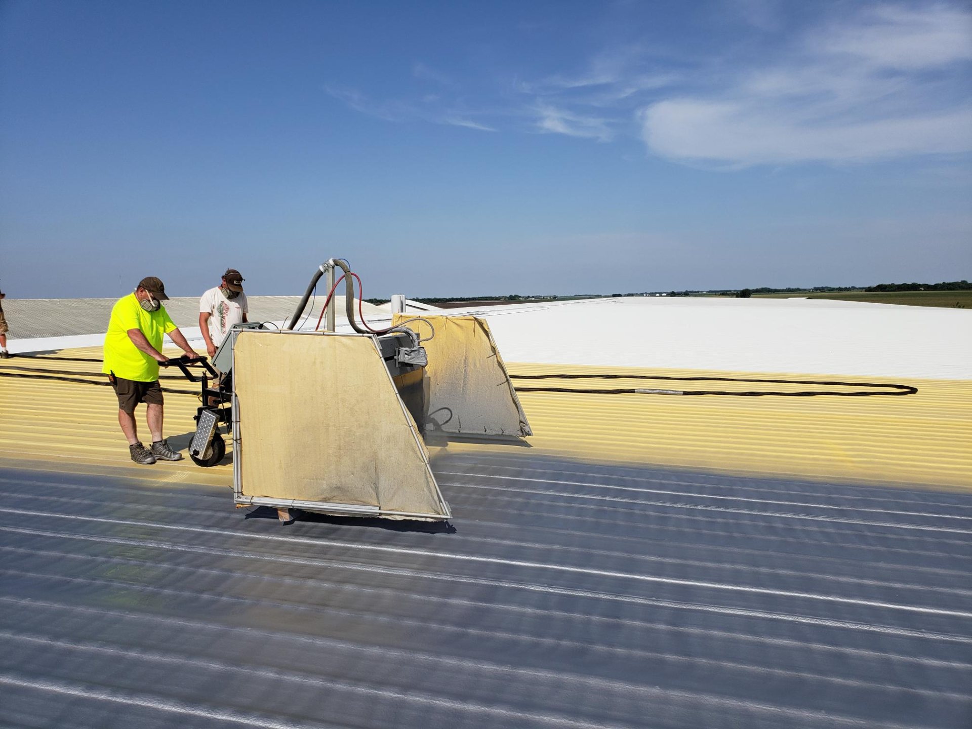 Two applicators spraying polyurethane foam roofing over a metal roof deck